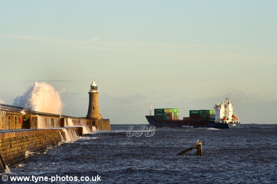 Waves breaking over the pier as the ship passes Tynemouth Lighthouse.