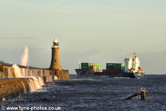 Waves breaking over the pier as the ship passes Tynemouth Lighthouse.